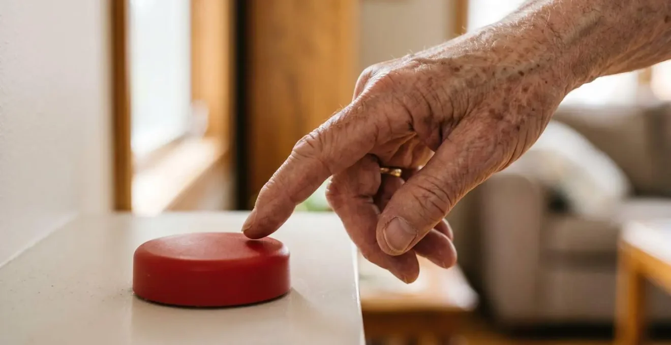 Gros plan sur une main hésitante au-dessus d'un bouton d'alerte médical symbolisant la décision d'appeler à l'aide