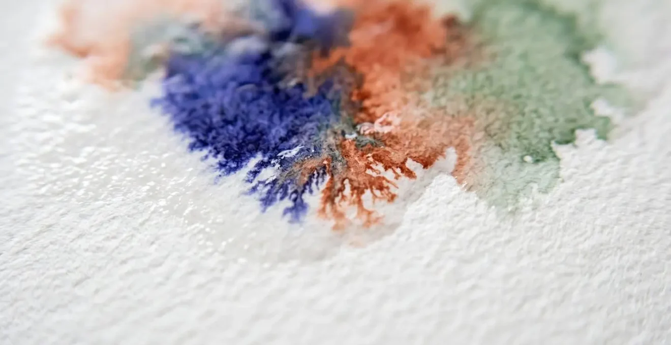 Fusion imprévisible de pigments aquarelle sur papier humide créant des effets organiques et spontanés