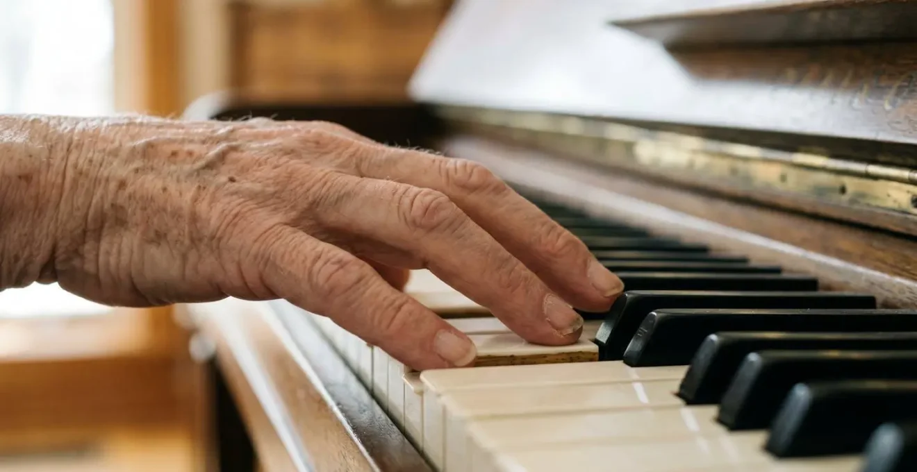 Gros plan sur les mains d'une personne senior posées sur un clavier de piano avec lumière naturelle douce